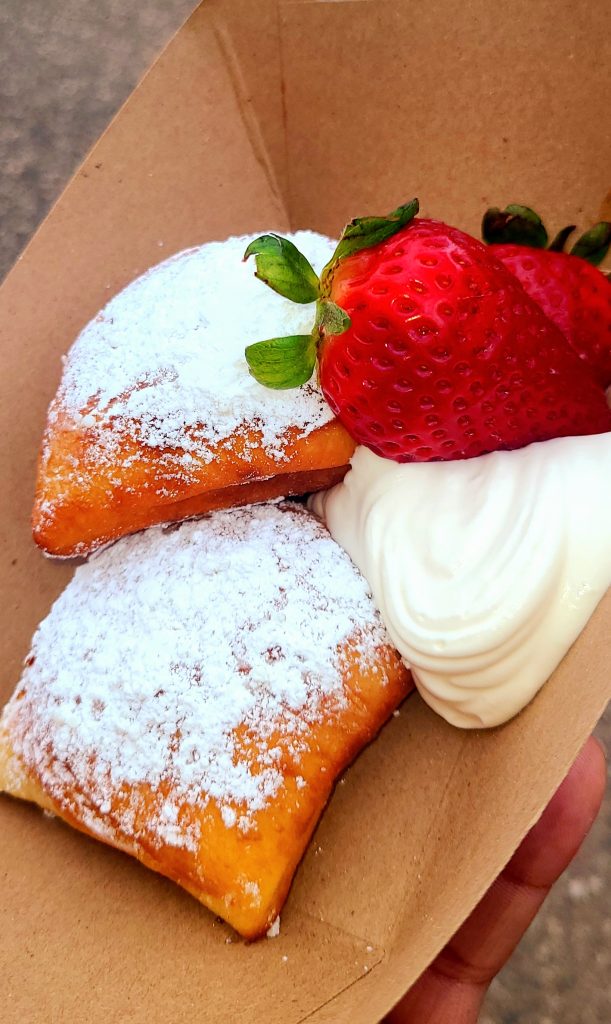 Photo of a beignet with strawberries and whipped cream.